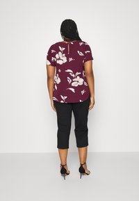Top corto a maniche corte bordeaux con schiena a chiave, abbinato a pantaloni neri a tre quarti e tacchi neri. Tessuto liscio con dettagli floreali.