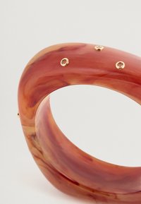 Ένα καμπύλο βραχιόλι φτιαγμένο από μαρμαρωμένη κόκκινη ρητίνη, με τέσσερα χρυσά στοιχεία που περιέχουν ενσωματωμένα πολύτιμα πετράδια, ομαλή υφή και γυαλιστερή επιφάνεια.