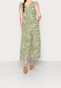 Salopette verde con motivo floreale, design senza maniche e schiena a V. Silhouette a gamba larga e vita cinchata, completata da sandali con tacco color tan.
