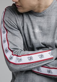 Graues karierter Langarmshirt mit kontrastierenden weißen und roten gestreiften Ärmeln, die schwarze Logos zeigen. Baumwollmischung, lässige Passform.