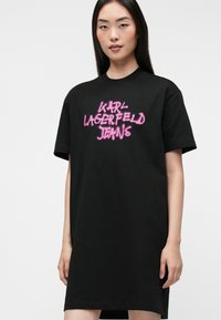 Czarna sukienka t-shirt wykonana z bawełny, z różowym napisem sprayowanym "KARL LAGERFELD JEANS" z przodu. Krótkie rękawy i luźny krój.