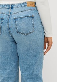 Light blue denim jeans with a medium rise, featuring two back pockets and a leather label with "VMD" at the waistband.