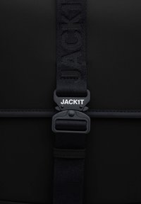Zaino nero con una tracolla testurizzata con il branding "JACK1T" e una chiusura robusta, progettato con un esterno elegante e minimalista.