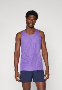 Lila Sporttanktop mit strukturiertem Mesh-Design, Rundhalsausschnitt und Logodetail, kombiniert mit marineblauen Shorts.
