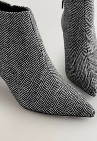 Blokhælede ankelstøvler i et sort-hvidt herringbone mønster. Har en spids tå og et stofmateriale med en tekstureret overflade.