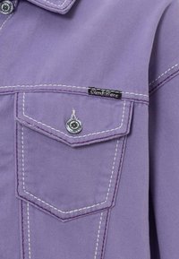 Lavendel Denimjacke mit kontrastierendem weißen Nähten, ausgestattet mit einer Brusttasche und einem Markenlabel in der Nähe der Tasche. Glänzendes Metallknopf-Detail.