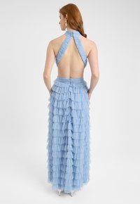 Vaalean sininen halterneck-mekko, jossa on röytiä, avoin selkä ja kerroksellinen hame salaisella vetoketjulla. Elegantti ja valuva muotoilu.