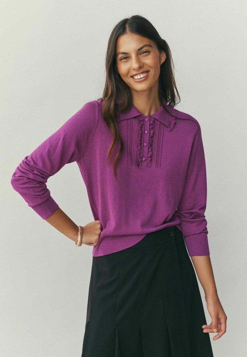 Purple knitted sweater with a buttoned placket and textured detailing, paired with a black skirt featuring a button accent.