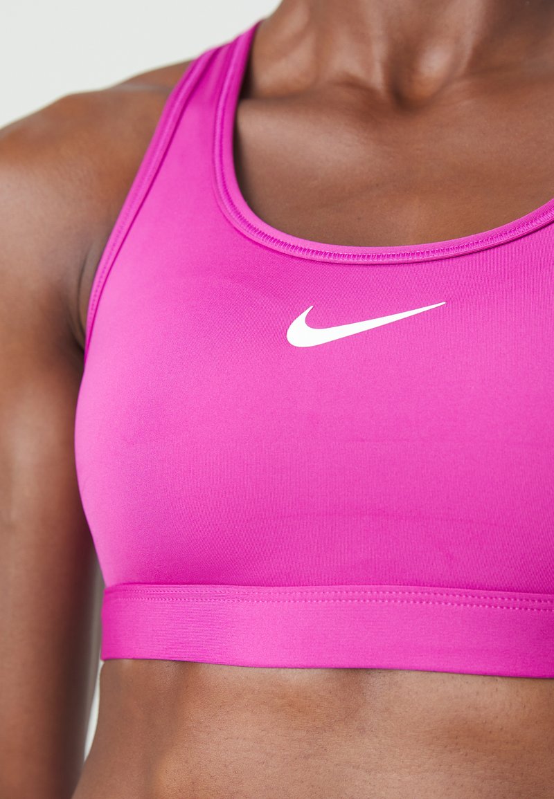 Nahaufnahme einer Person, die einen leuchtend pinken Nike-Sport-BH trägt und dabei den Oberkörper sowie das Logo auf der Brust zeigt.