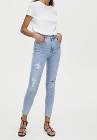 Jeans skinny azul claro con detalles desgastados y rasgados. Combinados con una camiseta blanca ajustada y sandalias negras con tiras.