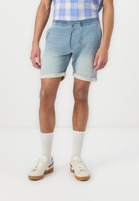 Pantaloni scurți din denim de culoare albastru deschis, cu talie cu șnur, manșete îndoite și buzunare laterale, asortați cu șosete albe și adidași bej.