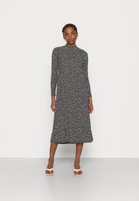 Vestido preto de mangas longas com estampa floral branca, decote alto, comprimento midi fluido e tecido suave. Combinado com sandálias brancas de tiras.