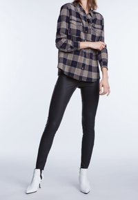 Chemise à carreaux bleu marine, beige et rouge ; associée à des leggings en cuir noir et des bottines blanches. Comprend des poches poitrine et des manches longues.