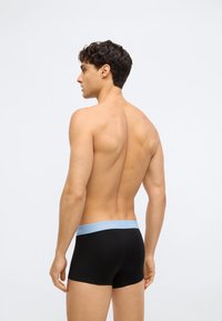 Juoda bokserių kelnių pora su šviesiai mėlyna elastinga juosta, ant kurios yra užrašas "Calvin Klein". Kelnių krova yra tvirtai prigludusi, o audinys yra glotnus ir malonus liesti.