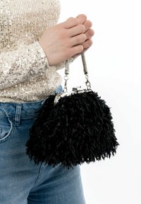 Svart väskor i fuskpäls med en texturerad, fluffig utsida. Har en silverfärgad metallram och kort kedjehandtag. Bärs med jeans och en paljettopp.