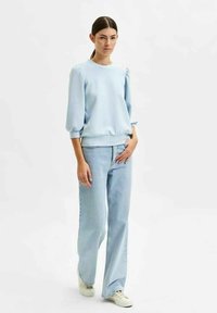 Light blue sweatshirt with puffed sleeves, paired with high-waisted, loose-fit light blue jeans and white sneakers. Simple and casual design.