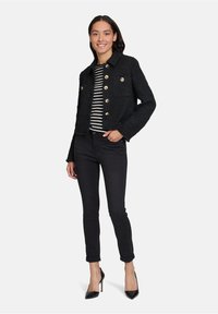 Czarna tweedowa kurtka z złotymi guzikami, krótki fason, dwie przednie kieszenie, noszona na czarno-białym pasiaku, zestawiona z czarnymi dżinsami i szpilkami.