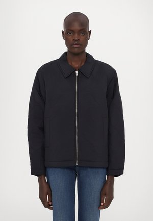 Veste matelassée noire avec col, fermeture éclair et poches latérales. Présente un motif texturé et une coupe décontractée. À associer avec un denim bleu.