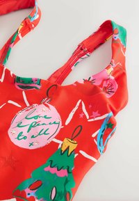Czerwony strój kąpielowy z świątecznym wzorem, przedstawiającym ozdoby choinkowe, gwiazdy i udekorowaną choinkę w żywych kolorach. Gładka, elastyczna tkanina.