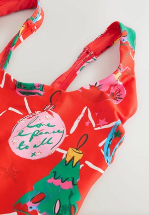 Piros fürdőruha ünnepi mintával, karácsonyi díszekkel, csillagokkal és élénk színű díszített fával. Simább, rugalmas anyagból.