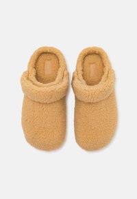 Chinelos fofos em tom de areia, com um exterior suave e texturizado, barra dobrada e um design minimalista. O interior também é forrado para maior conforto.