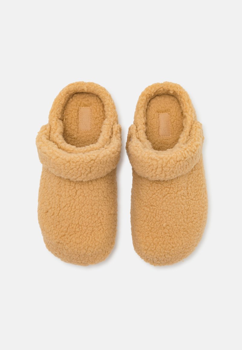 Chaussons en peluche marron avec un extérieur doux et texturé, un revers replié et un design minimaliste. L'intérieur est également doublé pour plus de confort.