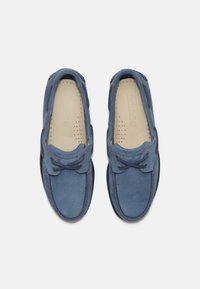 Niebieskie zamszowe buty na sznurówki z zaokrąglonym noskiem i kontrastującymi akcentami w kolorze granatu. Wewnątrz znajdują się perforowane detale zapewniające wentylację.