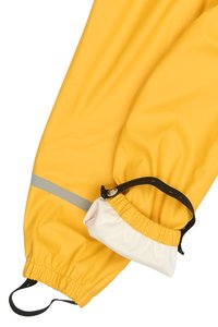 Pantalones impermeables amarillos con una textura suave, que cuentan con una franja reflectante gris y un puño elástico ajustable con una correa negra.