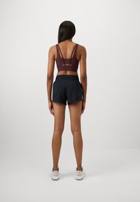 Soutien-gorge de sport bourgogne avec plusieurs bretelles, associé à un short noir. Présente un design ajusté et une texture douce et lisse. Des baskets blanches complètent la tenue.