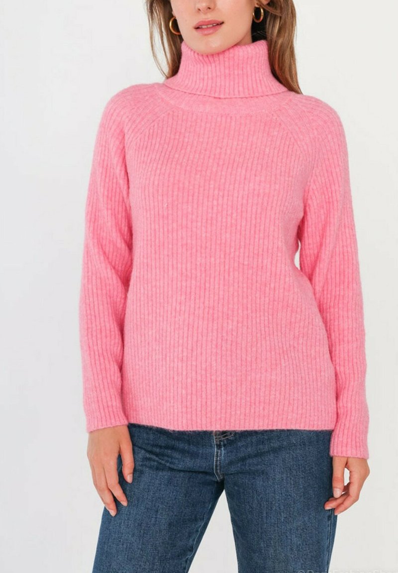 Pull en col roulé rose à côtes, avec de longues manches, présentant une texture douce et une coupe décontractée. Associé à un jean en denim bleu.