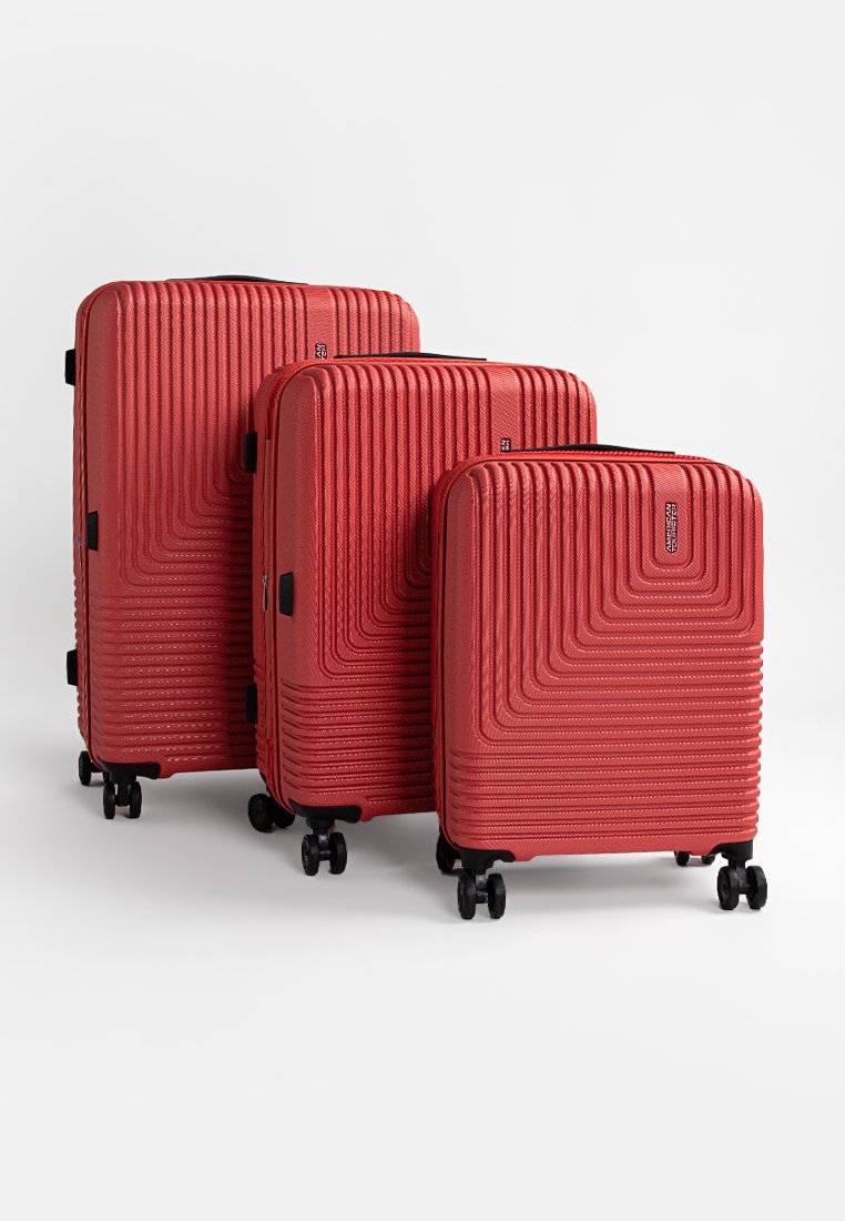 Trois valises rigides rouges de tailles variées avec des motifs géométriques texturés, chacune dotée de quatre roulettes pivotantes noires et de poignées latérales.