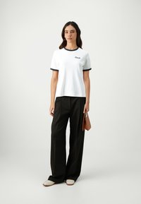 White short-sleeve T-shirt with black trim and "Coach" embroidered. Paired with high-waisted black trousers and cream slip-on shoes.