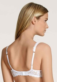 Witte kant BH met golvende randen, verstelbare bandjes en een haaksluiting, met intrigerende bloemenpatronen in het kant.