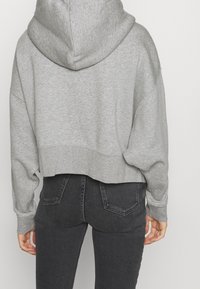 Hoodie gris coupé avec une grande capuche, une texture douce et des épaules tombantes, associé à un jean foncé taille haute.