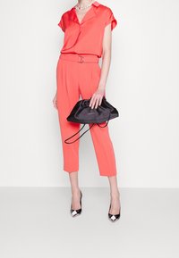 Korallfärgad satinblus med krage och korta ärmar, i kombination med högmidjade korallfärgade byxor. Svart satin dragstringväska och svarta klackskor.