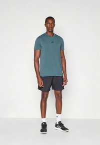 Pánský sportovní outfit zahrnující tričko s krátkými rukávy v tyrkysové barvě, černé kraťasy a černé tenisky s bílými detaily a logem.