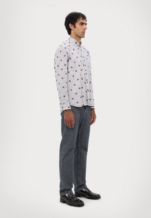 Gestreiftes Hemd mit kastanienbraunen Akzenten, graue Denim-Jeans und schwarze Slipper. Modell steht seitlich vor einem hellen Hintergrund.