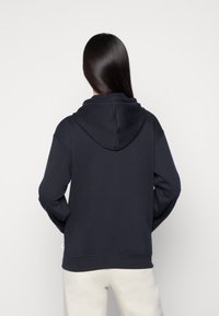 Sweat à capuche bleu marine en tissu doux, doté d'une poche kangourou à l'avant et de poignets et ourlet côtelés. Texture lisse et coupe décontractée.