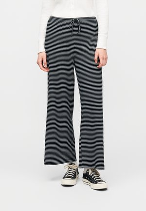 Osoba ubrana w czarno-białe szerokie spodnie w poziome paski z ściągaczem w pasie oraz czarne niskie trampki z białymi sznurowadłami.