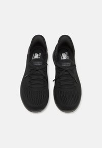 Juodos sportinės bateliai su tinklelio viršumi, apvaliu pirštu ir tekstūruotu padu. Yra raišteliai ir Skechers logotipas ant liežuvio.