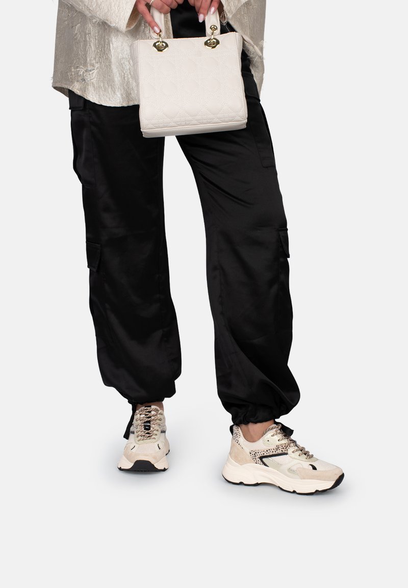 Pantalones cargo de satén negro, bolso de mano de un patrón beige claro y zapatillas beige con detalles de encaje y textura, llevados juntos.