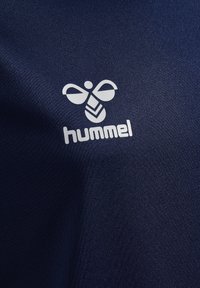 Camiseta deportiva azul marino con una textura suave, que presenta un logo de abeja blanca y la marca "hummel" en la parte inferior.