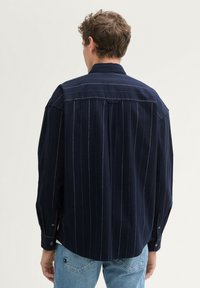 Camicia a righe blu navy con colletto button-down e maniche lunghe, caratterizzata da una vestibilità rilassata e un tessuto leggermente testurizzato.