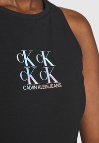 Musta hihaton paita, jossa on pyöreä pääntie ja etuosassa helmiäisen hohtoinen logo-teksti "CK Calvin Klein Jeans". Sileä pinta.