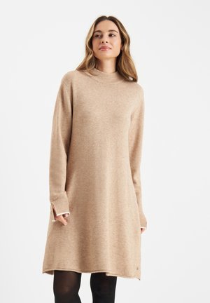 Beige gebreide jurk met hoge hals, lange mouwen en zijsplitsen. Zachte textuur en een ontspannen pasvorm. Accentuatie met een klein logo.