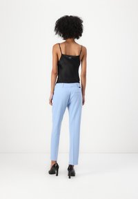 Black satin camisole with thin straps, paired with light blue tailored pants and black high heels. Focus on sleek, smooth textures.