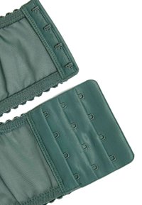 Prenda de tela verde con bordes ondulados, que presenta ganchos de metal en un lado y un panel liso en el otro, para un cierre ajustable.