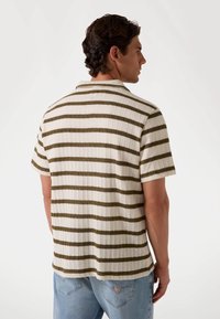 Polo de manga corta en color crema con rayas verde oliva. Tejido texturizado con un acabado acanalado, con cuello clásico y un corte relajado.