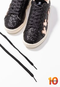 Baskets noires pailletées avec des lacets noirs et des patchs beige en forme de Mickey Mouse sur les côtés, posées sur une surface blanche.