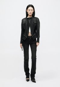 Casaco de couro preto com corte curto, ferragens metálicas e dois bolsos frontais. Combinado com calças de ganga pretas e sapatos de salto fino com ponta afunilada.